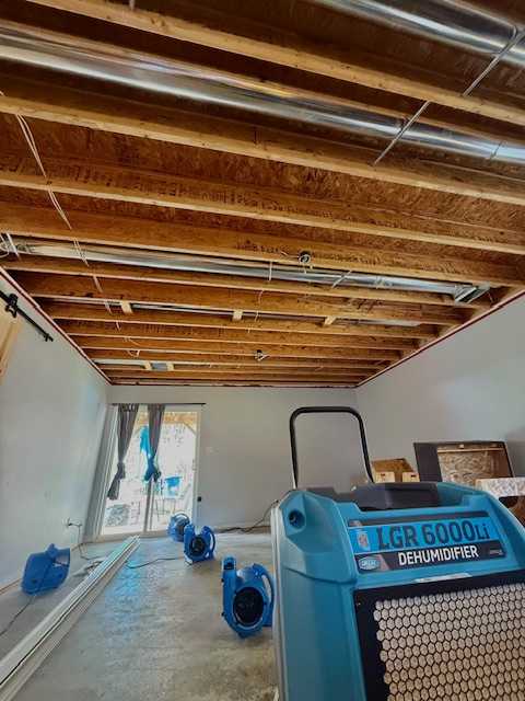 Dehumidifier and air movers drying a room with exposed ceiling framing